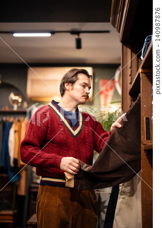 Handsome stylish guy choosing velvet jeans from display in fashionable vintage selective shop. Handsome stylish guy choosing velvet jeans from display in fashionable vintage selective shop. 140987876