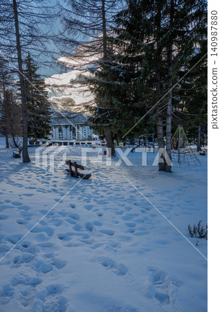 Sestriere, piedmont, italy. December 8, 2024. Sestriere, italy, playground covered in snow, featuring a bench and trees, with mountains and buildings in the background Sestriere, piedmont, italy. December 8, 2024. Sestriere, italy, playground covered in snow, featuring a bench and trees, with mountains and buildings in the background 140987880