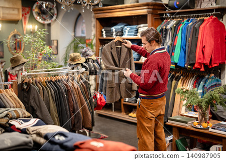Classy man deciding on purchasing vintage wool blazer in men's apparel second hand boutique. Classy man deciding on purchasing vintage wool blazer in men's apparel second hand boutique. 140987905