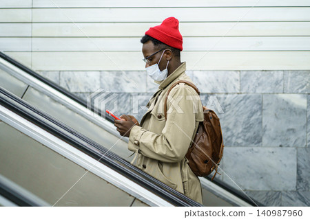 Black man stands on escalator in subway, wear face mask to protect from contact with flu virus Black man stands on escalator in subway, wear face mask to protect from contact with flu virus 140987960