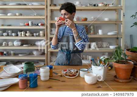 Young creative artisan crafts woman drinking morning coffee from handmade mug and eating croissant Young creative artisan crafts woman drinking morning coffee from handmade mug and eating croissant 140987970