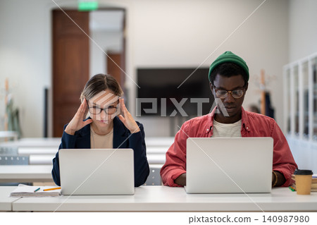Concentrated serious students learning sitting in desktop in college lecture classroom with laptops. Concentrated serious students learning sitting in desktop in college lecture classroom with laptops. 140987980