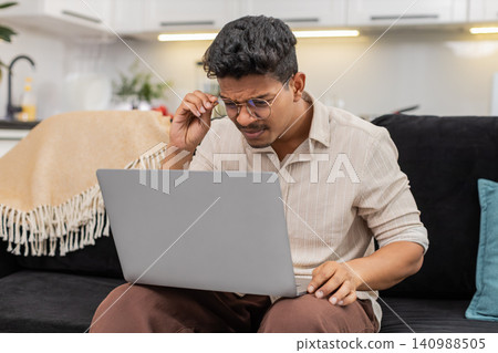 Indian man puts on glasses for clear reading of small notebook text vision focus resumes daily work Indian man puts on glasses for clear reading of small notebook text vision focus resumes daily work 140988505