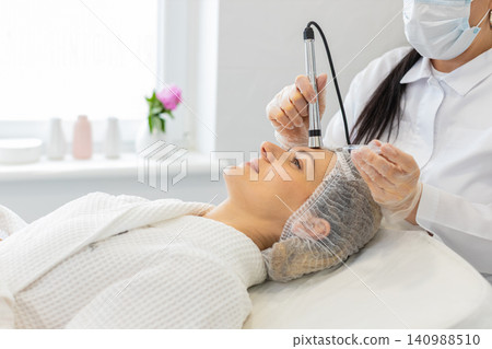 Cosmetologist performs injection-free mesotherapy with electroporation on woman at cosmetic clinic 140988510
