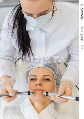 Beautician uses microcurrent device for anti age face therapy on woman in beauty clinic spa indoors Beautician uses microcurrent device for anti age face therapy on woman in beauty clinic spa indoors 140988515