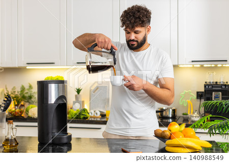 Arabian young adult man pouring fresh brewed coffee in home kitchen morning caffeine addiction daily Arabian young adult man pouring fresh brewed coffee in home kitchen morning caffeine addiction daily 140988549