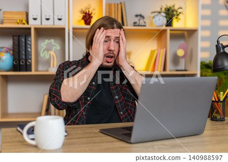Young man on home table reacting to bad laptop result with stress frustration and loss from bad news Young man on home table reacting to bad laptop result with stress frustration and loss from bad news 140988597