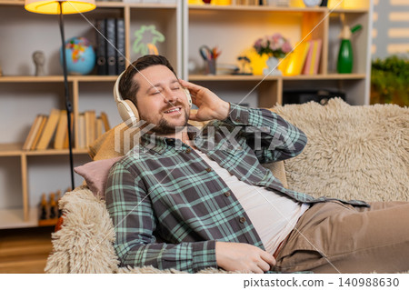 Young man on home sofa meditating with wireless headphones and calm smile during quiet music break Young man on home sofa meditating with wireless headphones and calm smile during quiet music break 140988630