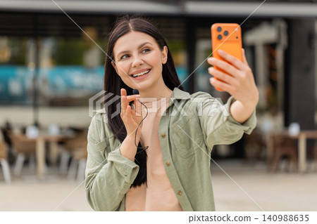 Young woman filming location review walking in city street with smartphone using lavalier microphone Young woman filming location review walking in city street with smartphone using lavalier microphone 140988635