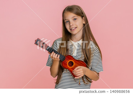 Little child girl kid playing toy ukulele smiling while enjoying imaginary concert performance 140988656