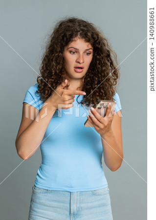Woman surprised scrolling news on smartphone raising eyebrows amazed expression unexpected shock Woman surprised scrolling news on smartphone raising eyebrows amazed expression unexpected shock 140988661