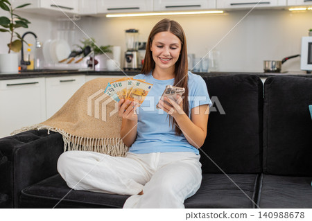 Young woman counts euro money cash with smartphone checks exchange rate plans purchase invests bonus Young woman counts euro money cash with smartphone checks exchange rate plans purchase invests bonus 140988678