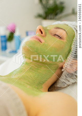 Caucasian woman lying with dried green peeling mask on face and neck during beauty clinic spa care Caucasian woman lying with dried green peeling mask on face and neck during beauty clinic spa care 140988681