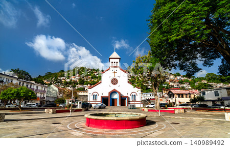 The white facade of Saint Anthony of Padua Catholic Church in Fort-de-France, Martinique with colorful hillside houses in the background under a blue sky. The white facade of Saint Anthony of Padua Catholic Church in Fort-de-France, Martinique with colorful hillside houses in the background under a blue sky. 140989492