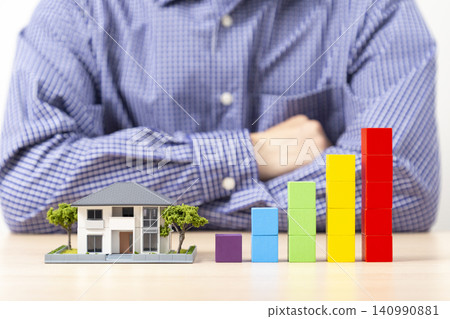 A man with his arms crossed, surrounded by a graph made of building blocks and a model house. A man with his arms crossed, surrounded by a graph made of building blocks and a model house. 140990881