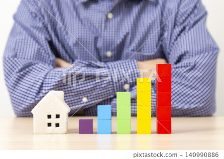 A man with his arms crossed, surrounded by a graph made of building blocks and a model house. A man with his arms crossed, surrounded by a graph made of building blocks and a model house. 140990886