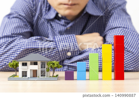 A man with his arms crossed, surrounded by a graph made of building blocks and a model house. A man with his arms crossed, surrounded by a graph made of building blocks and a model house. 140990887