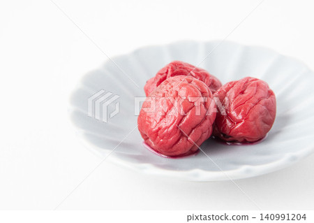 A bright red pickled plum placed on a small plate A bright red pickled plum placed on a small plate 140991204
