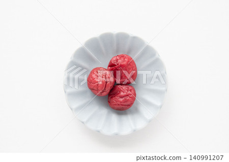 A bright red pickled plum placed on a small plate A bright red pickled plum placed on a small plate 140991207