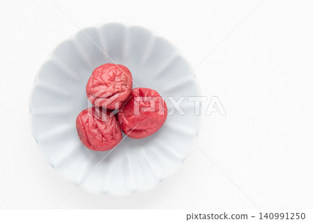 A bright red pickled plum placed on a small plate A bright red pickled plum placed on a small plate 140991250