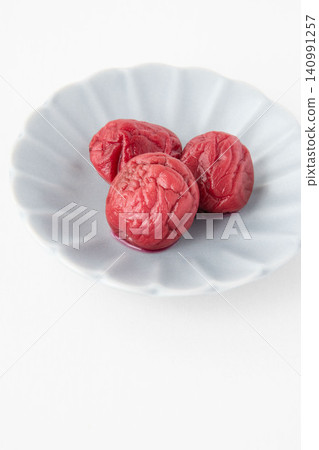 A bright red pickled plum placed on a small plate A bright red pickled plum placed on a small plate 140991257