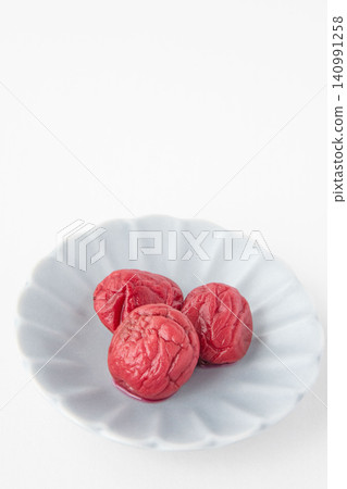 A bright red pickled plum placed on a small plate A bright red pickled plum placed on a small plate 140991258