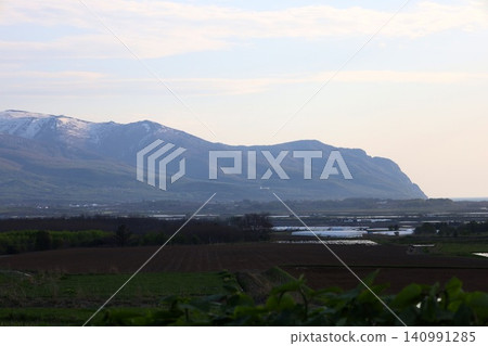 In spring in Hokkaido, the Niseko mountain range and Raiden Coast viewed from the vicinity of Horikabu River in Kyowa Town, at the base of the Shakotan Peninsula in Shiribeshi, at dusk. In spring in Hokkaido, the Niseko mountain range and Raiden Coast viewed from the vicinity of Horikabu River in Kyowa Town, at the base of the Shakotan Peninsula in Shiribeshi, at dusk. 140991285