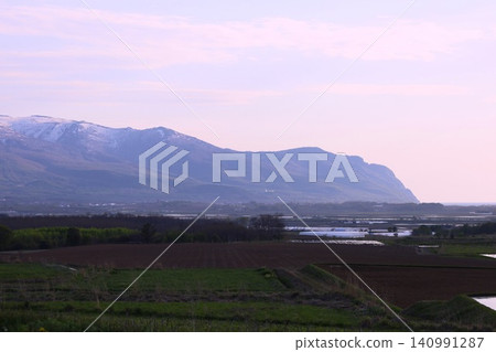 In spring in Hokkaido, the Niseko mountain range and Raiden Coast viewed from the vicinity of Horikabu River in Kyowa Town, at the base of the Shakotan Peninsula in Shiribeshi, at dusk. In spring in Hokkaido, the Niseko mountain range and Raiden Coast viewed from the vicinity of Horikabu River in Kyowa Town, at the base of the Shakotan Peninsula in Shiribeshi, at dusk. 140991287