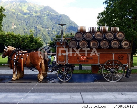 A traditional horse-drawn carriage carrying barrels travels through the town of Interlaken, Switzerland. A traditional horse-drawn carriage carrying barrels travels through the town of Interlaken, Switzerland. 140991618