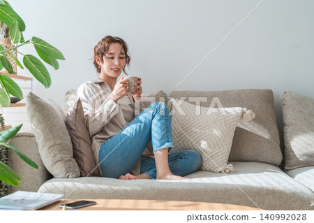 時尚女性坐在沙發上喝熱飲 140992028
