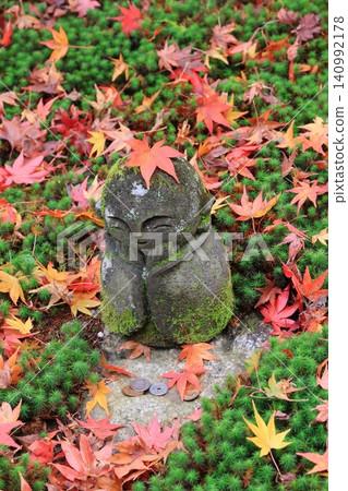 A Jizo statue surrounded by fallen maple leaves. 140992178