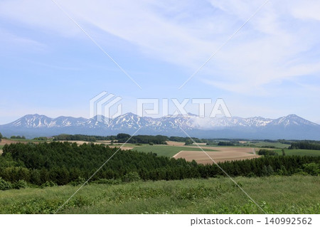 Hokkaido in June, Hokkaido in spring, Hokkaido in early summer: The town of Biei and the Tokachi Mountain Range viewed from the Northwest Hill Observation Park in Biei, a town of rolling hills. 140992562