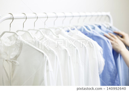 A woman's hands pick up clothes hanging on a rack. 140992640