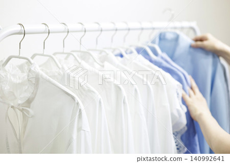 女人的手拿起掛在衣架上的衣服。 女人的手拿起掛在衣架上的衣服。 140992641