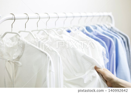 女人的手拿起掛在衣架上的衣服。 140992642
