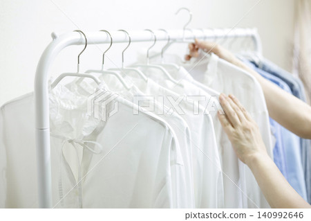 A woman's hands pick up clothes hanging on a rack. A woman's hands pick up clothes hanging on a rack. 140992646