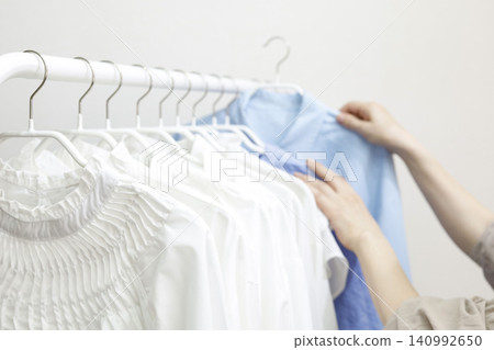 A woman's hands pick up clothes hanging on a rack. 140992650