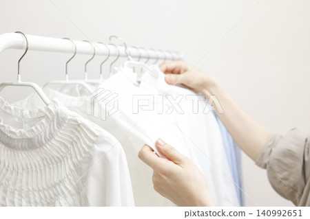 女人的手拿起掛在衣架上的衣服。 140992651
