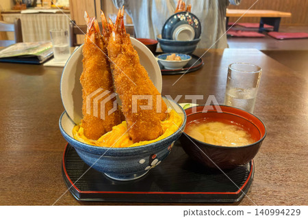 A set meal of rice bowl topped with three large fried shrimp and egg. A set meal of rice bowl topped with three large fried shrimp and egg. 140994229