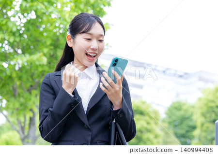 A woman in a business suit looking at her smartphone during her job search. 140994408