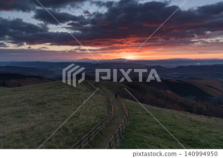 A fenced path stretches across a pasture at sunset. 140994950