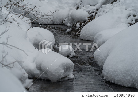 Snow piled on the rocks and a dark stream Snow piled on the rocks and a dark stream 140994986
