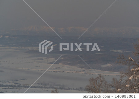 A pale plain shrouded in winter haze and white mountain ranges. A pale plain shrouded in winter haze and white mountain ranges. 140995001