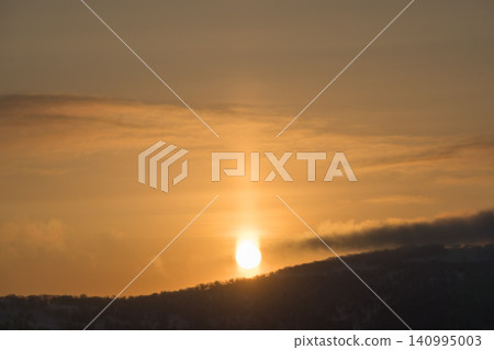 An orange sun pillar rising over a dark ridgeline An orange sun pillar rising over a dark ridgeline 140995003