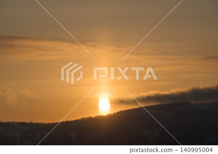 An orange sun pillar rising over a dark ridgeline 140995004