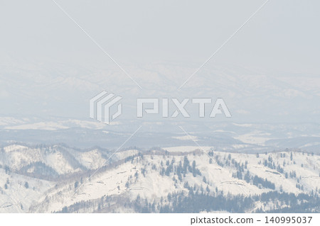 A snow-covered ridgeline and sparse forest shrouded in a faint mist. 140995037