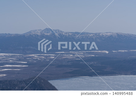 A vast, frozen caldera lake surrounded by forested hills. A vast, frozen caldera lake surrounded by forested hills. 140995488
