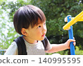 A two-year-old boy, an Asian toddler of Japanese descent, playing on playground equipment in a park. 140995595