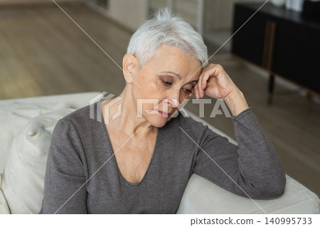 Sad tired ill sick lonely disappointed older senior woman sitting at home alone. Unhappy mature grandmother experiencing grief relative death bad news. Stressed elder lady suffering from loneliness Sad tired ill sick lonely disappointed older senior woman sitting at home alone. Unhappy mature grandmother experiencing grief relative death bad news. Stressed elder lady suffering from loneliness 140995733