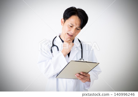 一位身穿白大褂的中年男醫生一邊看著裝有病人病歷的活頁夾，一邊沉思。 140996246